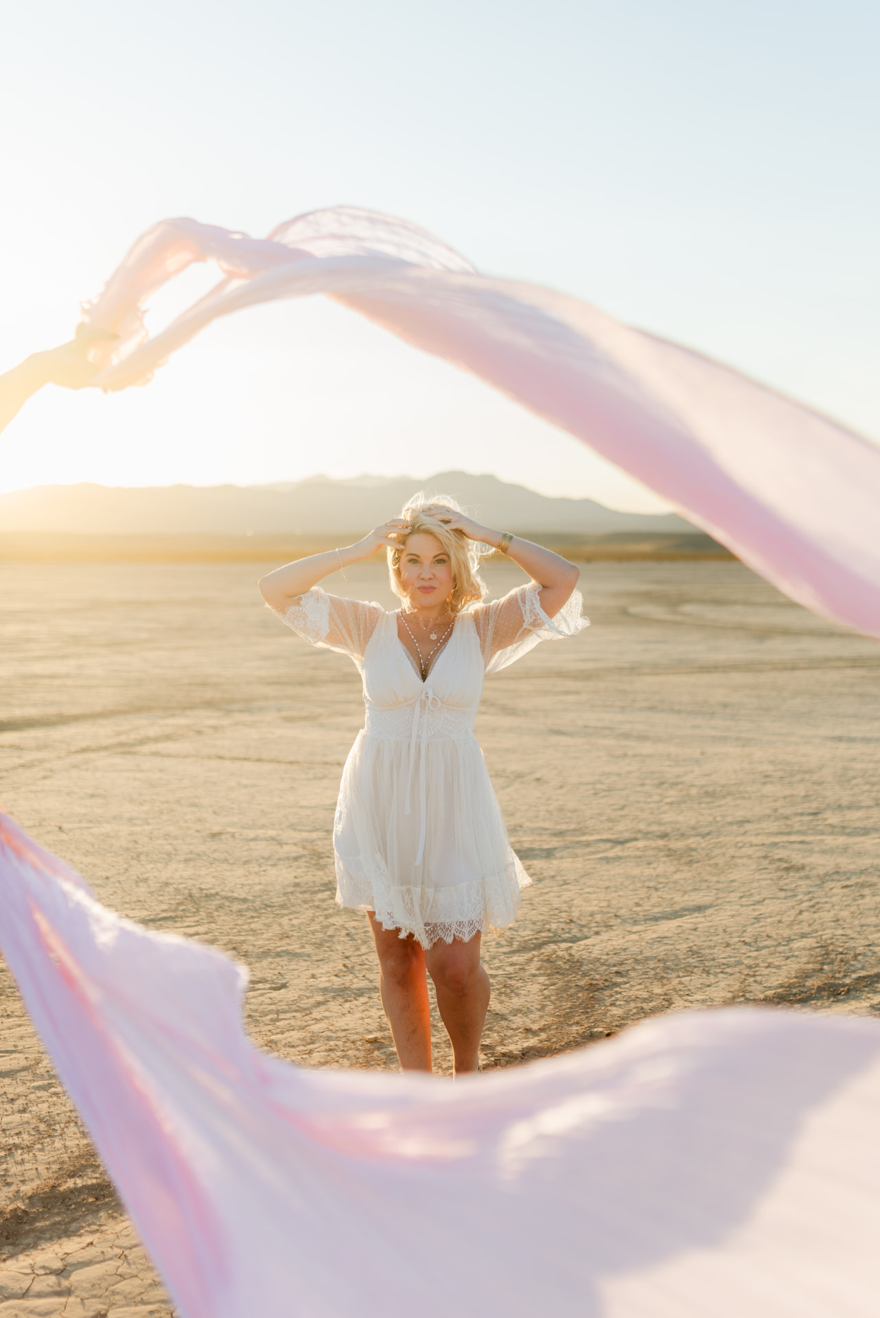 Nina Moon in a white dress on the desert flats at golden hour, pink silk drifting through the air